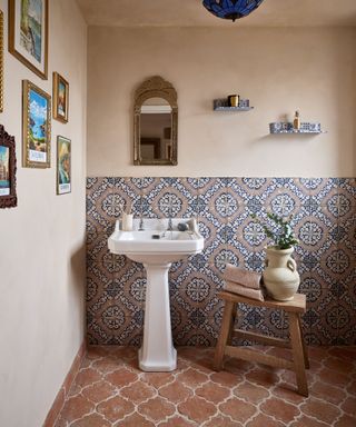 A small bathroom with terracotta floor tiles and patterned porcelain tiles of the wall and plaster pink paint on the rest of the walls and ceiling