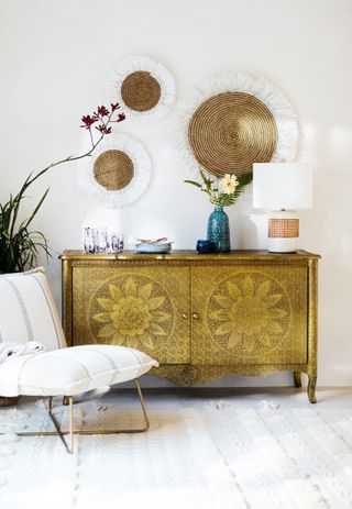 Textured woven wall hangings on decorative gold chest with white relaxed chair