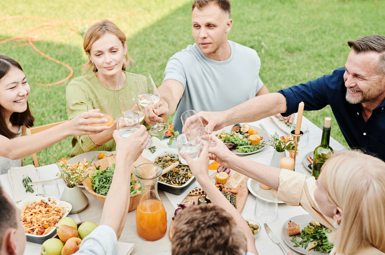 A group of people eating at a table outside raising their wine glasses