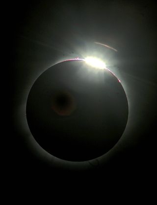 A bead of the sun's disk emerges from behind the moon during a total solar eclipse.