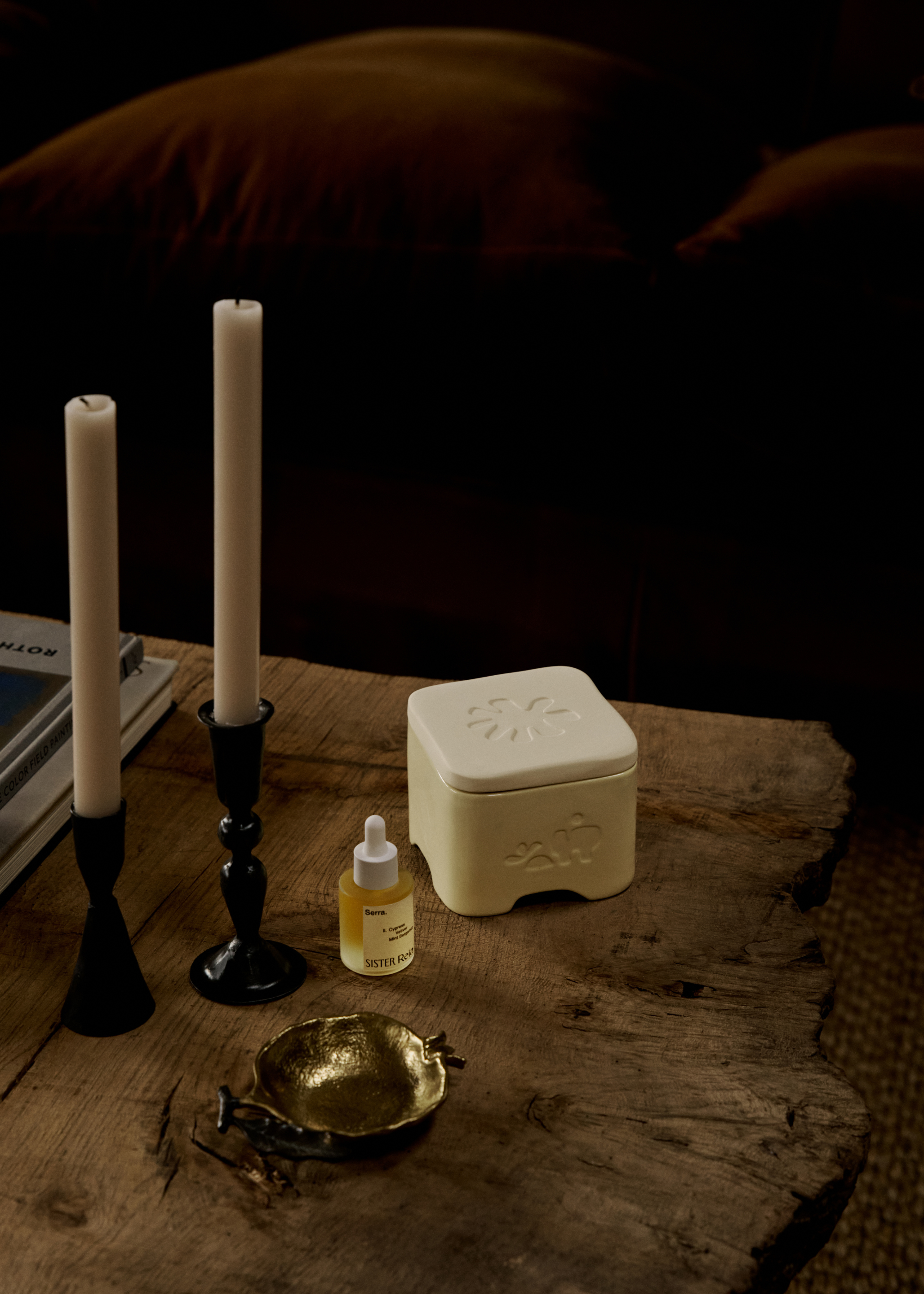A ceramic diffuser box beside a bottle of essential oils, and a pair of candle sticks on a coffee table