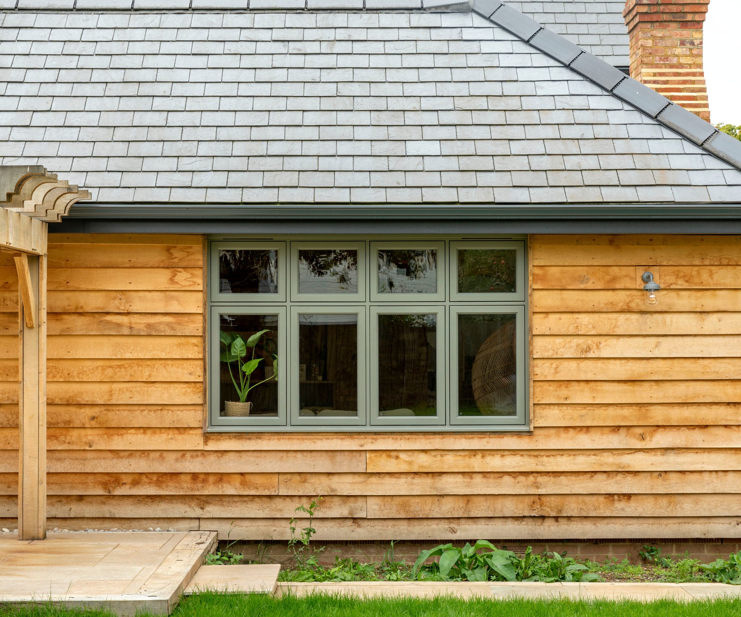 Modern timber-clad home with sage green framed windows and slate roof.