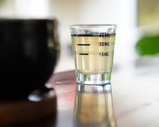 Measuring glass with vinegar-looking liquid inside on a shiny wooden kitchen surface