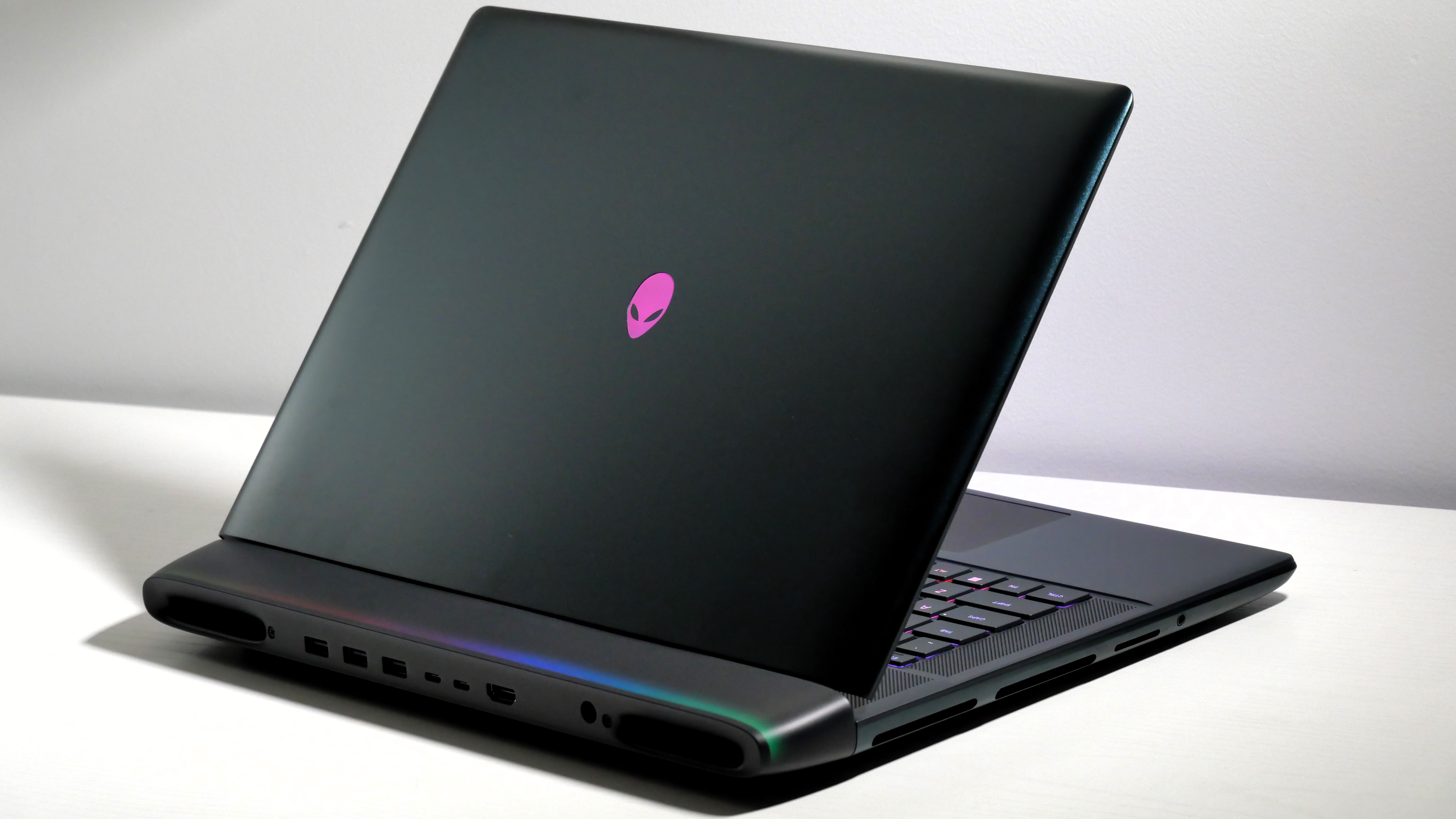Alienware 16 Area-51 (RTX 5080) open at an angle on a white desk, highlighting the keyboard, lid, and light bar on the hinge.