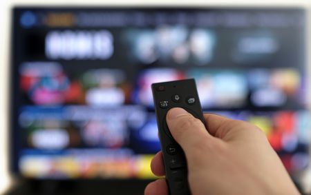 A picture of a hand holding a remote control and a television in the background