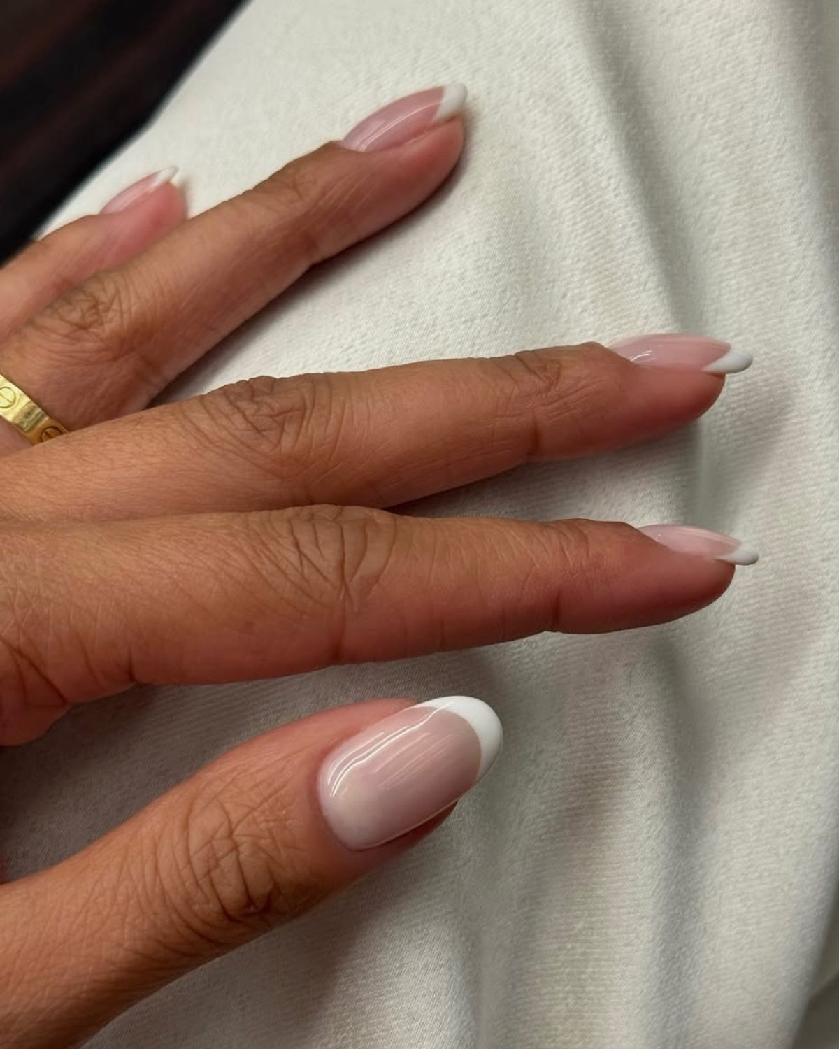 A model wears a classic pink-toned, white-tipped French manicure on a hand with a single gold ring