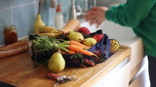 Fruit and vegetables sitting on chopping board next to woman washing her hands