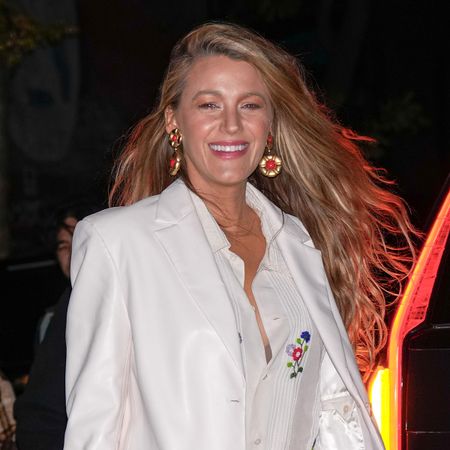 Blake Lively at a screening of "Wicked" on December 3, 2024, in New York wearing a white blazer, Bode shirt, Levi's 501 vintage jeans, blue socks, red Marc Jacobs sequin platform Mary-Jane heels, and a white Chanel flap bag. Her hair is worn down and wavy and she's wearing red earrings.