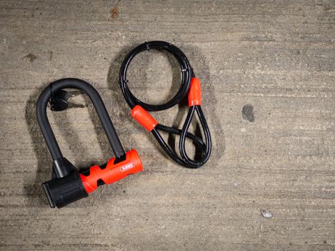 A black and red Abus Ultimate 420 lock and cable on a stone floor next to a bike rack