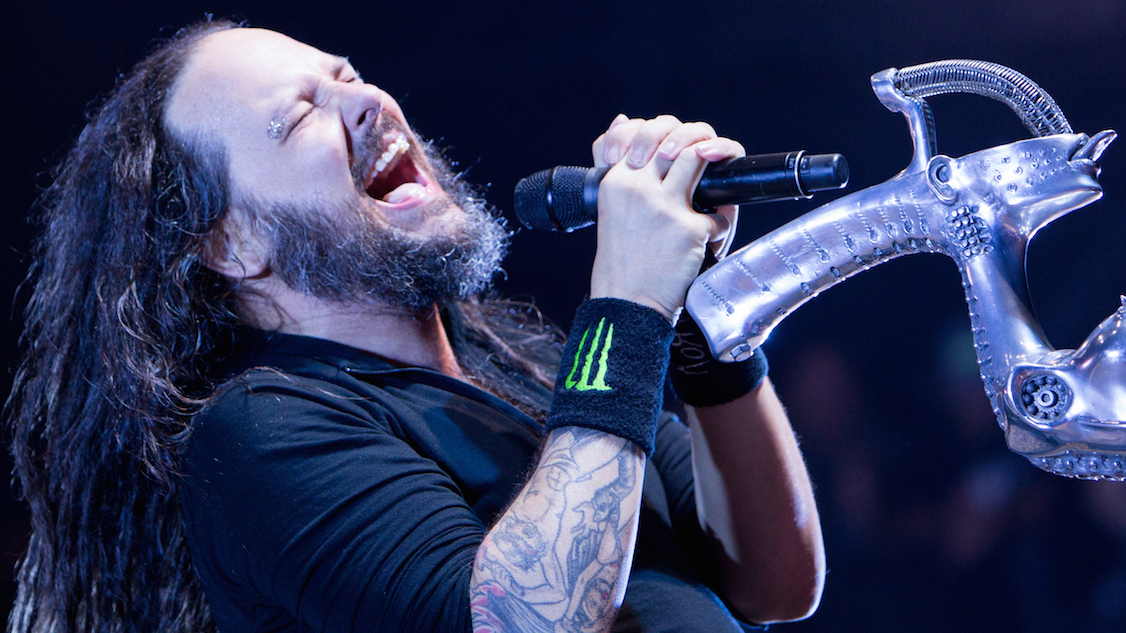 Korn&#039;s Jonathan Davis leaning back form his mic stand and singing with his eyes closed.