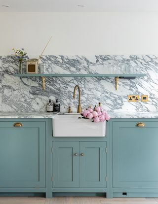 blue kitchen cabinets with butler sink and marble splashback and worktops