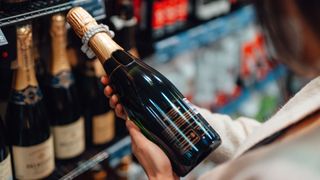 Woman checking label on prosecco or champagne bottle at liquor store
