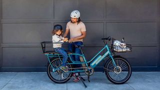 A parent stood in front of a garage next to their Blix Bike with their child sitting on the back