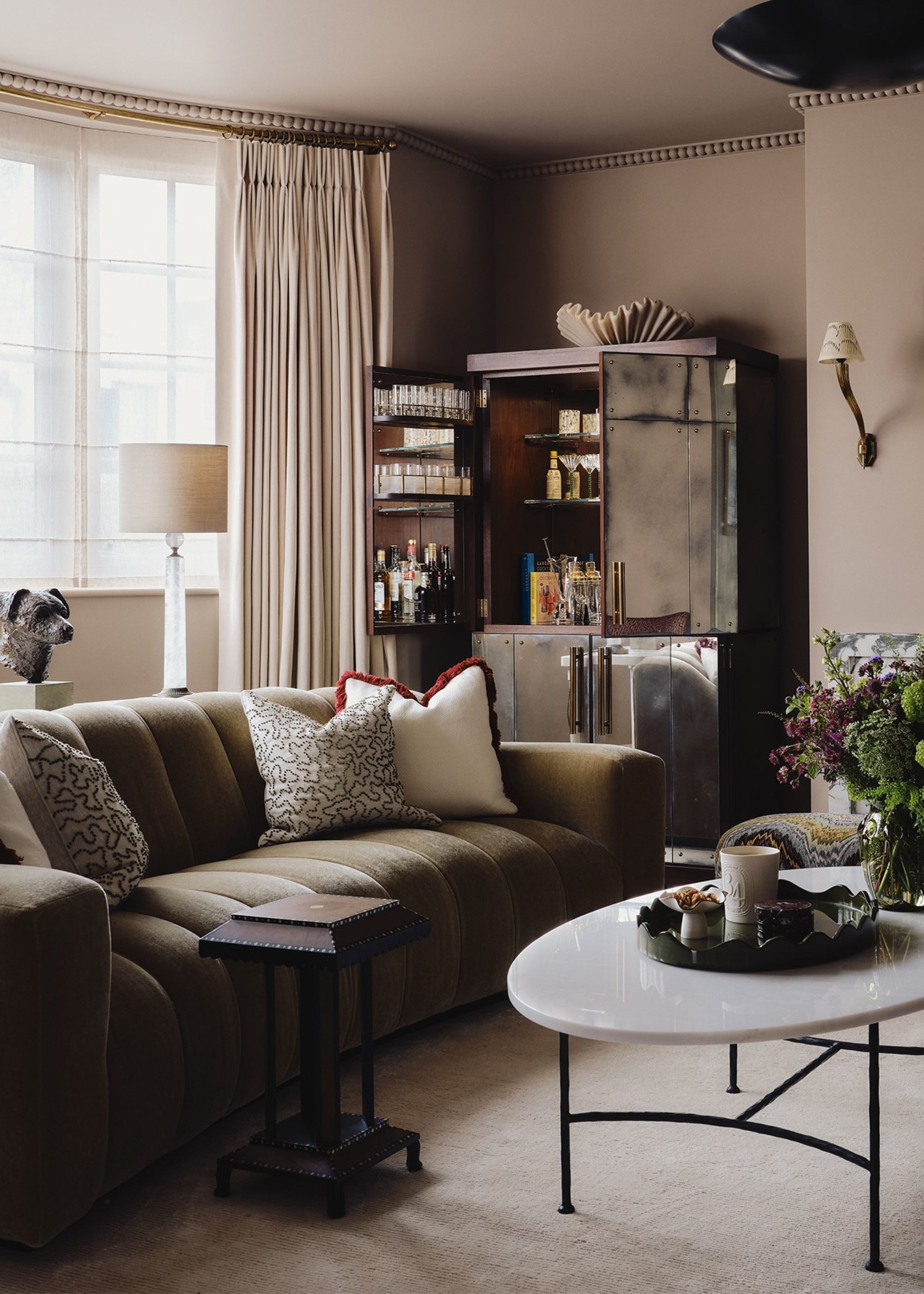 A living room with plaster pink walls, a large, olive green sofa, and a mirrored cabinet in the corner with drinks inside.