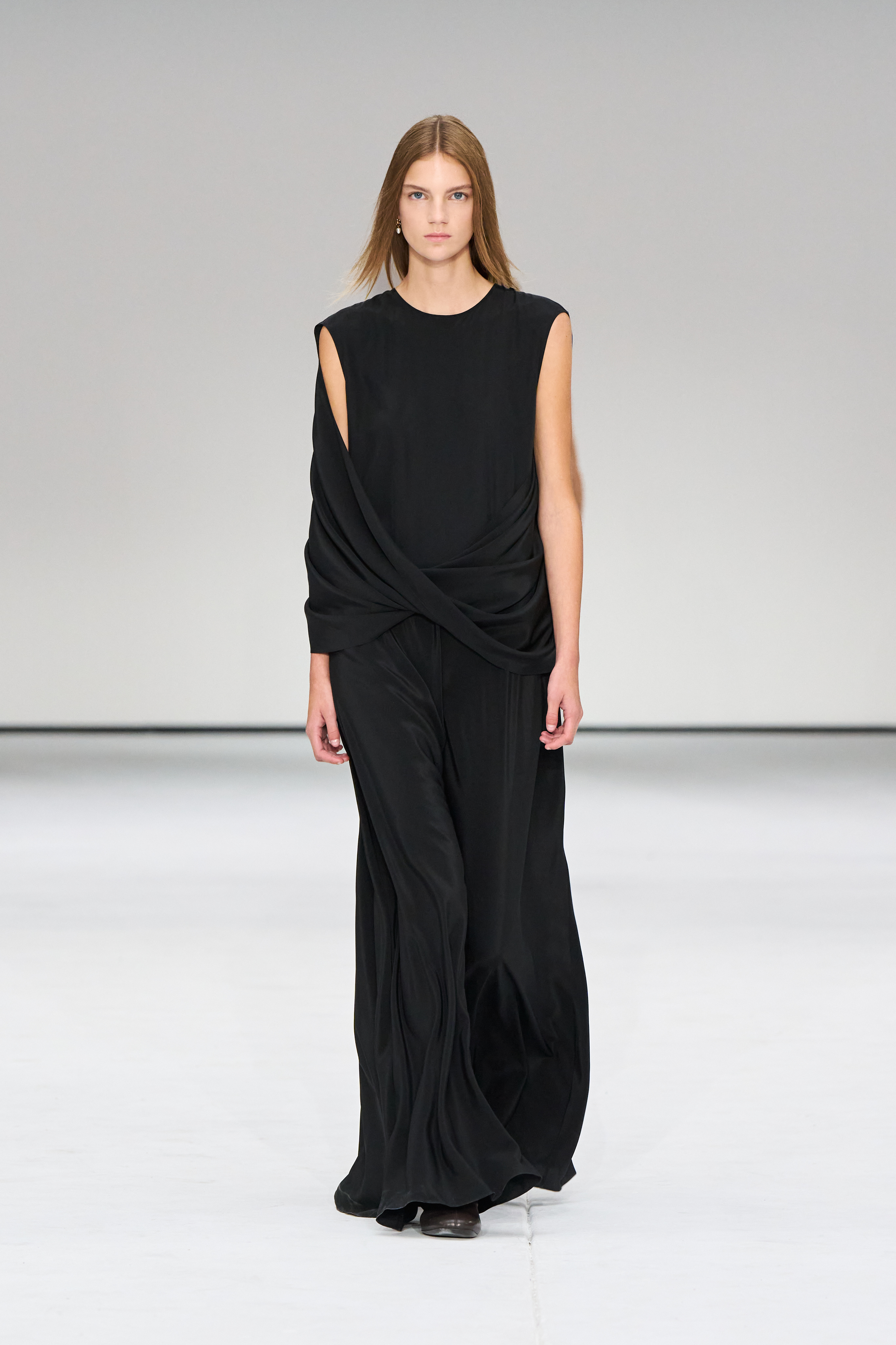 A woman wears a long black draped maxi dress.
