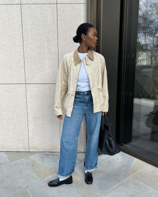 Woman wearing barn jacket, white t-shirt, jeans, and black loafers taking outfit photo.