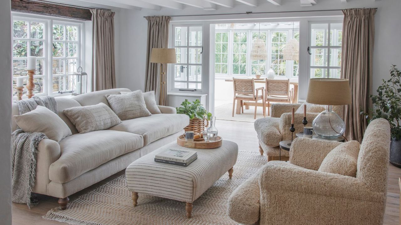 A neutral living room with floor to ceiling curtains around the doors and windows. 