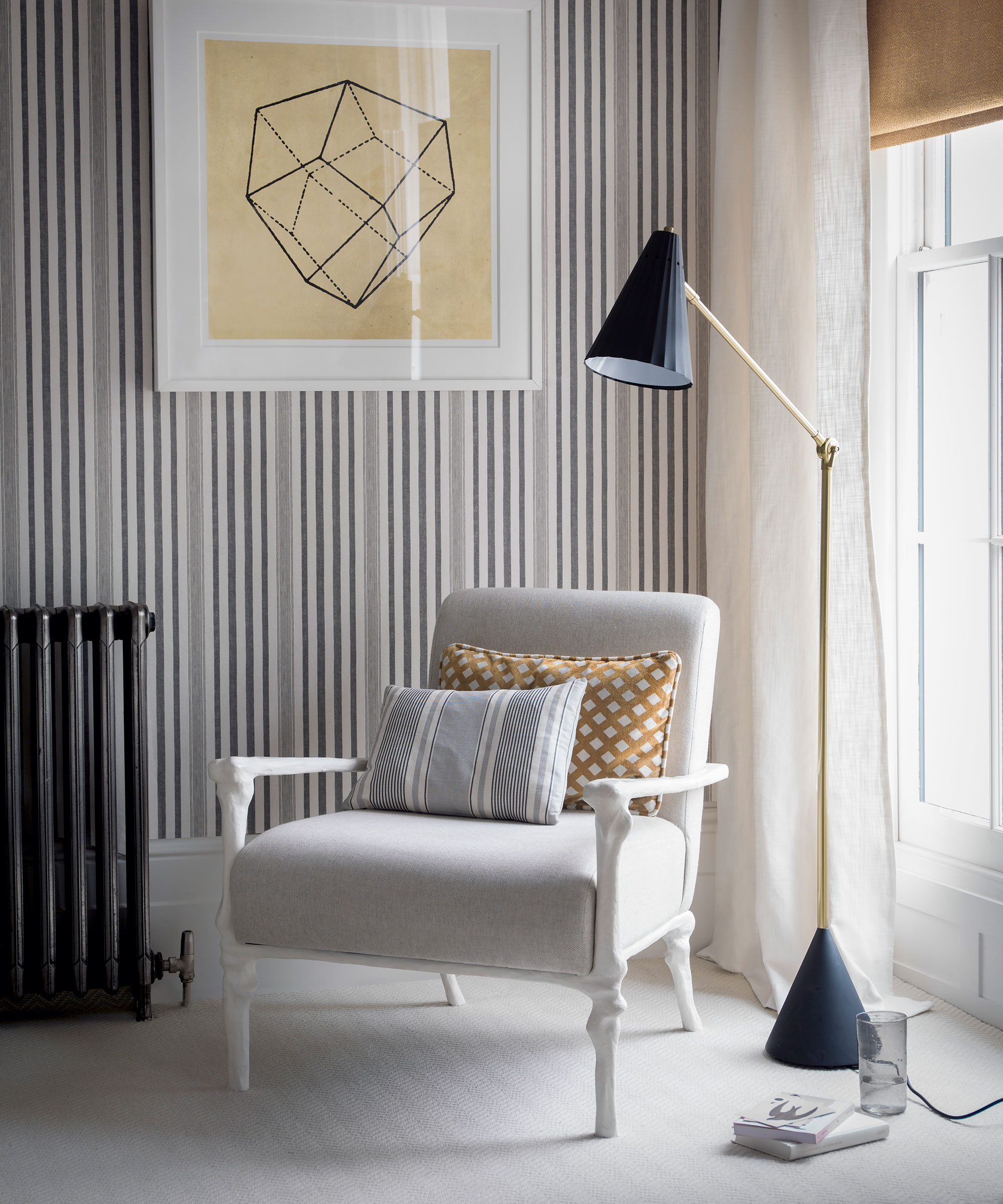 An example of bedroom lighting ideas showing a black floor lamp next to an armchair and striped wallpaper