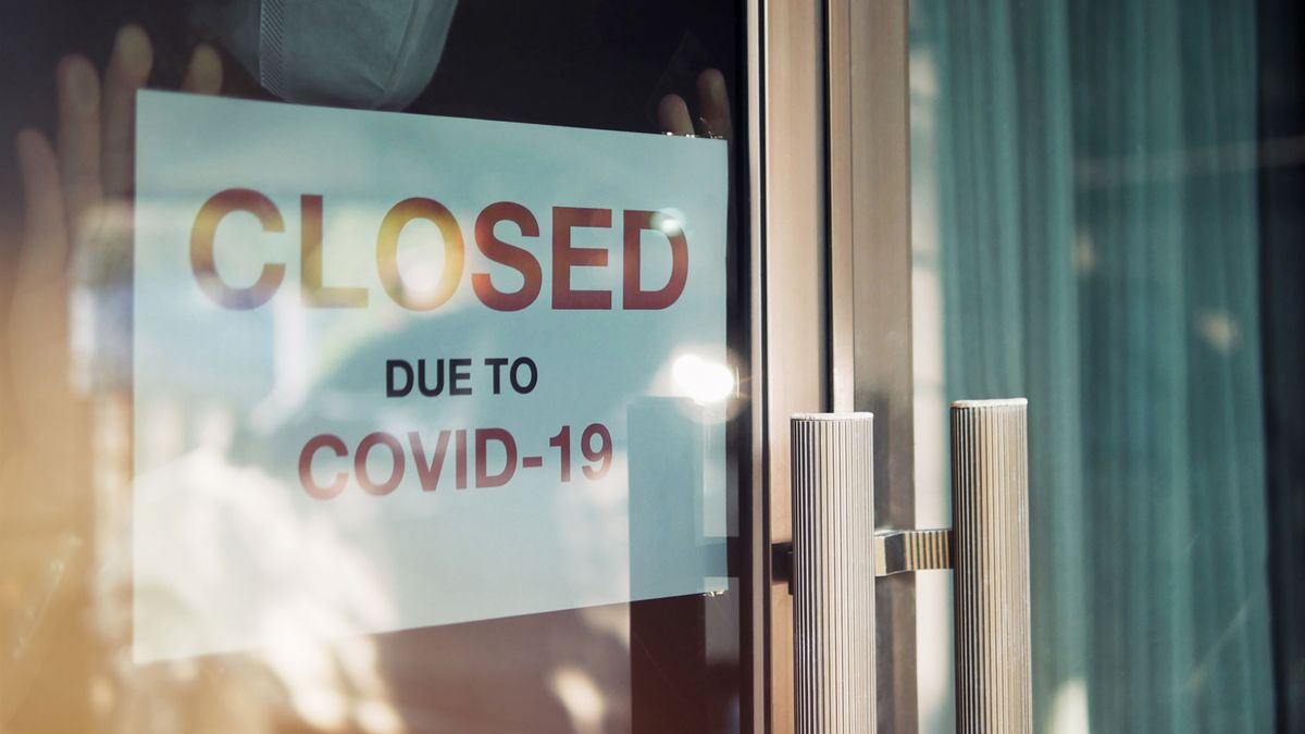 Unidentified person wearing mask hanging closed sign on front door