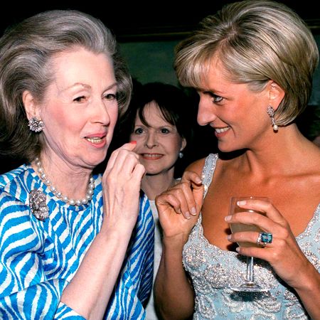 Princess Diana wearing a blue dress, holding a wine glass and smiling at her stepmother, Raine Spencer