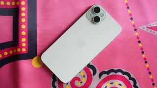 iPhone 15 Plus i vitt ligger på en rosa mönstrad duk.