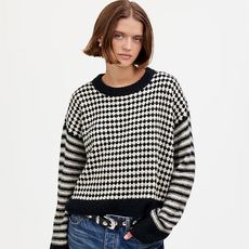 model wears black and white sweater with stripes on sleeves and diamonds on torso and jeans with a studded belt