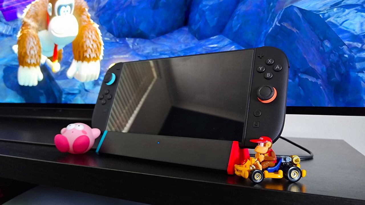 SIWIQU dock with Switch 2 attached next to Kirby figure and Diddy Kong Mario Kart car with Donkey Kong Bananza gameplay in backdrop.