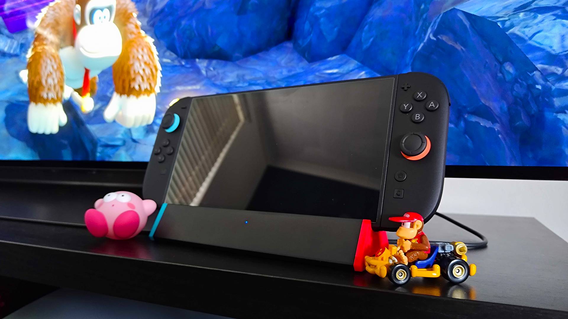 SIWIQU dock with Switch 2 attached next to Kirby figure and Diddy Kong Mario Kart car with Donkey Kong Bananza gameplay in backdrop.