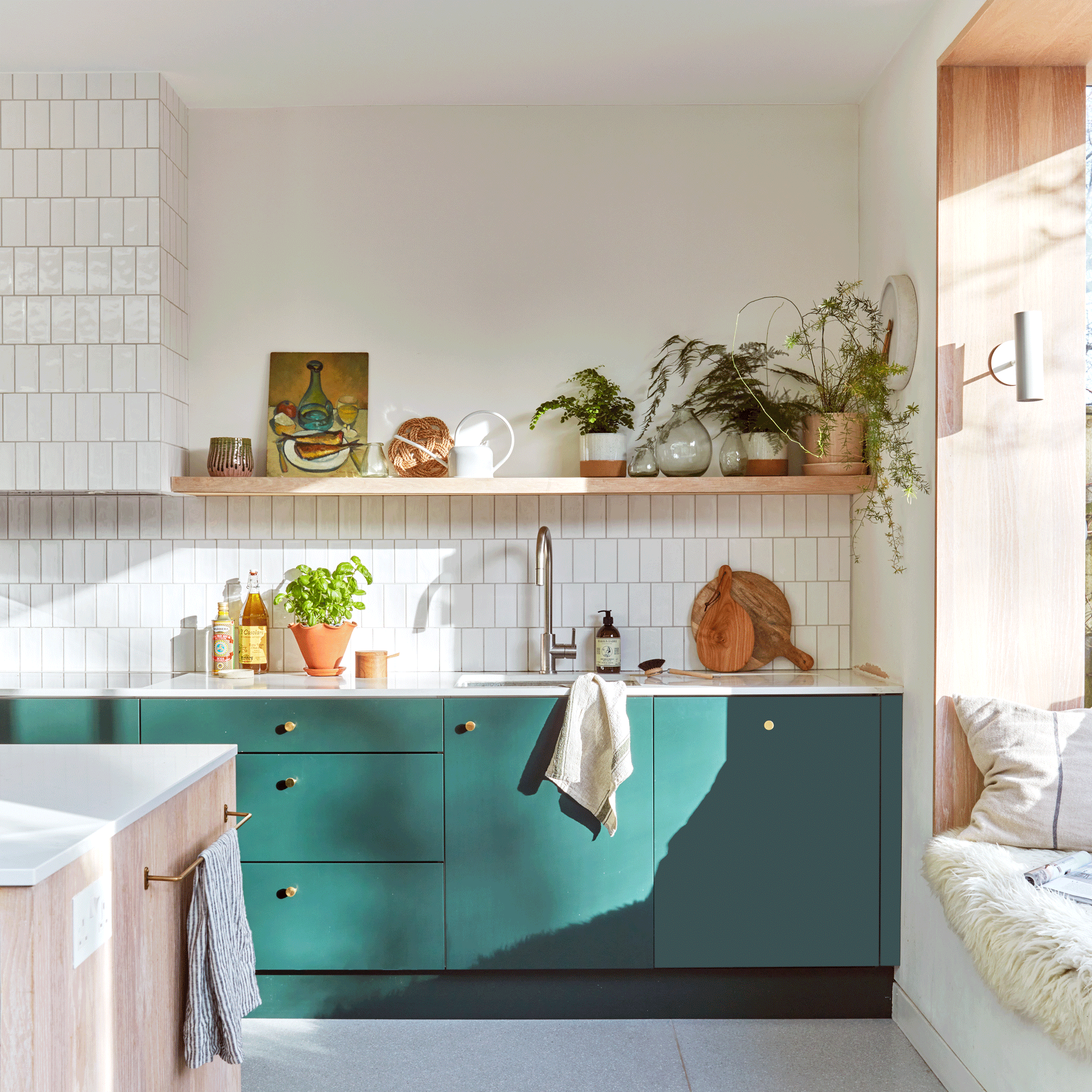 a kitchen with green cabinetry and white tiled walls beside a sunny window seat