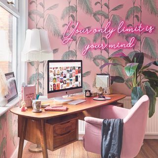 Home office with pink tropical wallpaper and neon sign.
