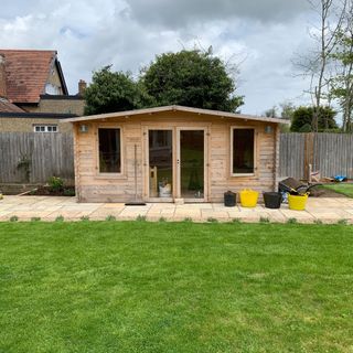 Wooden summer house on patio area next to green grass lawn in garden