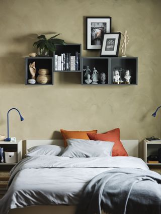 bedroom with beige textured walls, box shelving above bed, gray and orange bedding