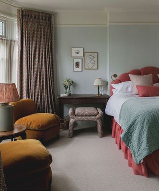 light blue painted bedroom with a pink bed, mustard velvet armchairs and dark wood bedroom furniture