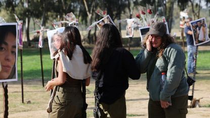 An Israeli soldier wipes her tears as she stands with fellow troops in front of pictures of people taken captive or killed by Hamas militants during the Supernova music festival on October 7