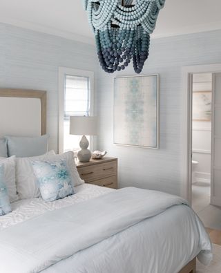 pale blue bedroom with beaded shades of blue chandelier, ensuite, textured blue wallpaper, pale blue bedding and cushions, side table, artwork