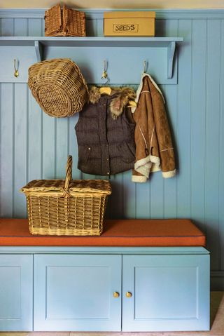 mud room boot room with blue cabinetry and coat and hats hanging up and basket on bench seat