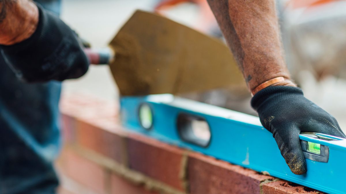 hands laying brick wall using trowel and blue spirit level