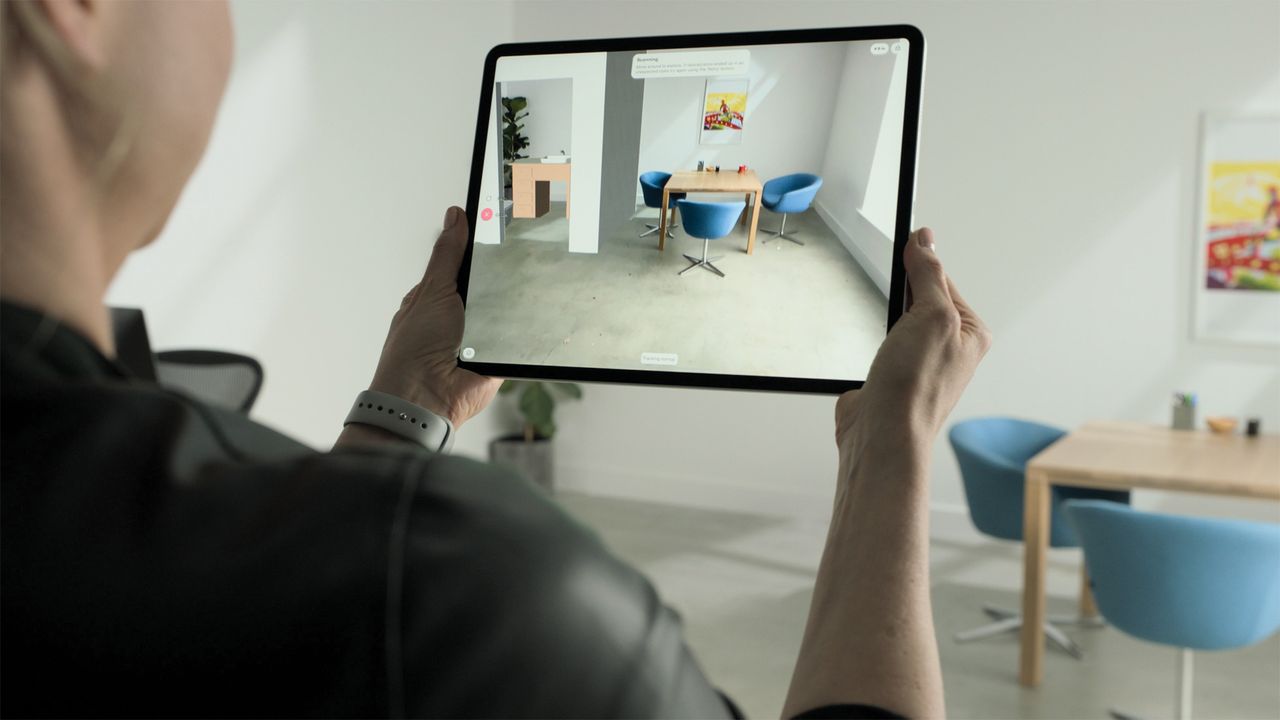 A man holding up an iPad in a dining room space