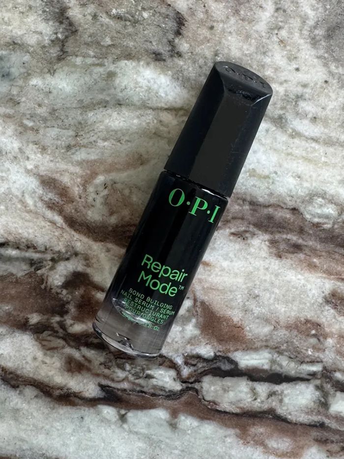 The OPI Repair Mode Bond Building Nail Treatment Serum on a marble background