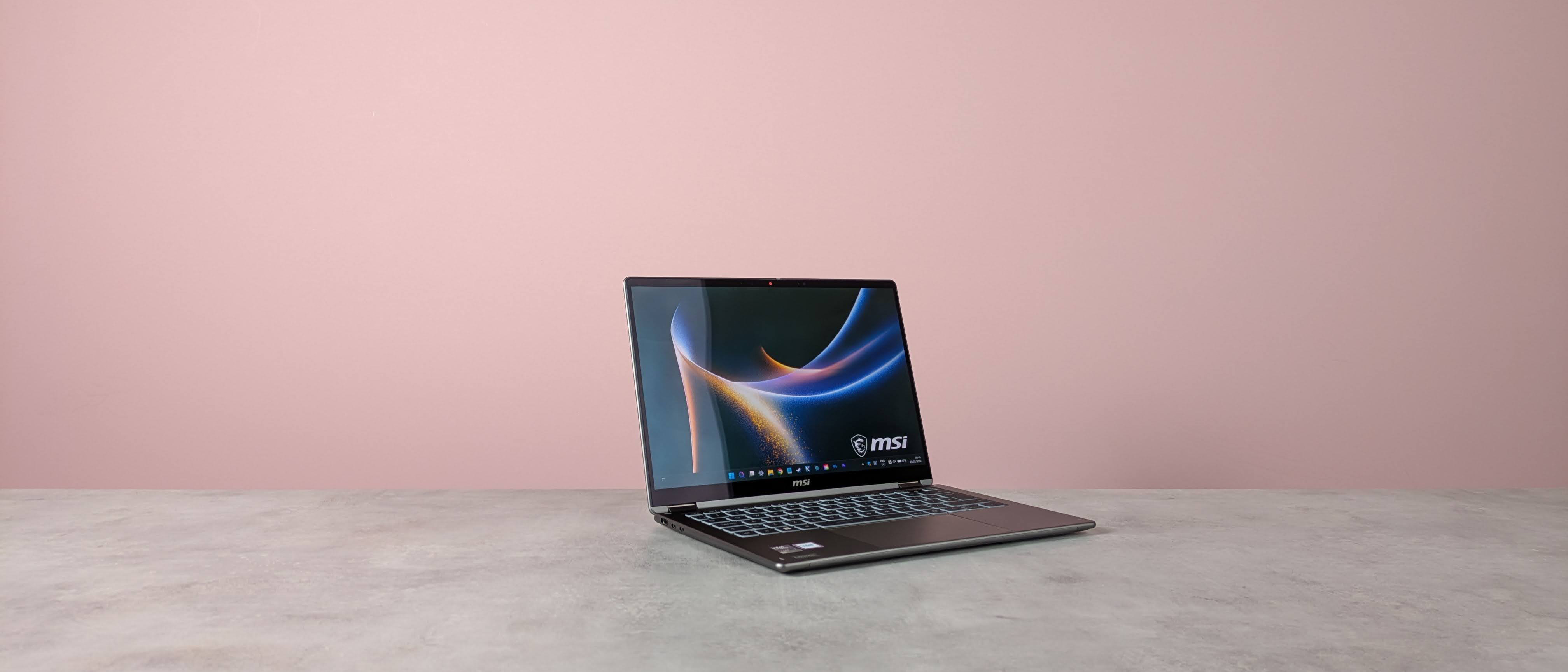 Three-quarter view of MSI Prestige 14 Flip AI+ open on white desk with pink wall in background