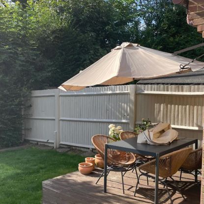 Garden fence painted in Cuprinol Garden Shades Natural Stone next to raised decking area with outdoor seating and beige parasol