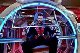 A man sits in a chair with a red harness and looks at futuristic screens on a circular structure in front of him, in 'The Expanse.'