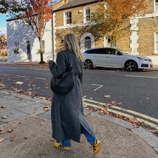 Fashion influencer Lucy Williams on the street wearing a long grey winter coat, blue jeans, and yellow sneakers with a Bottega Veneta bag.