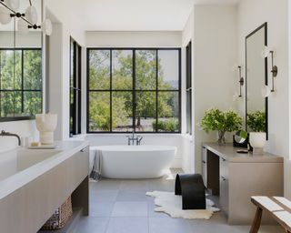 A large en suite with a white bath below a large triple aspect window with black frames