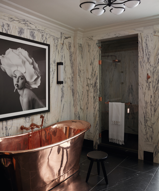 copper bathtub with artwork behind and marble walls with shower and pendant light
