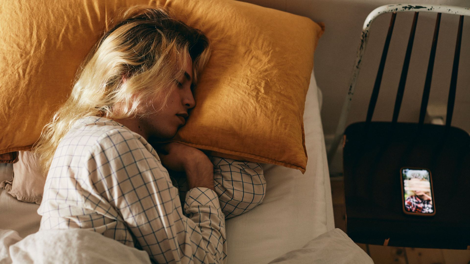A person with long blonde hair lying on their side sleeping with their arms tucked up against their chest in the 't-rex' sleeping position