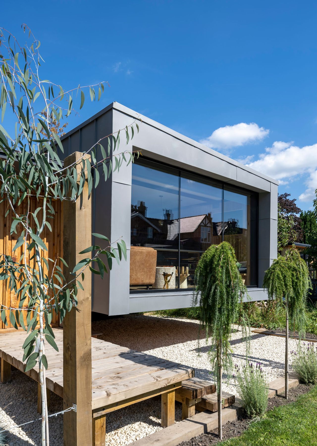 The exterior of a tiny home with a large glazed window surrounded by shrubbery