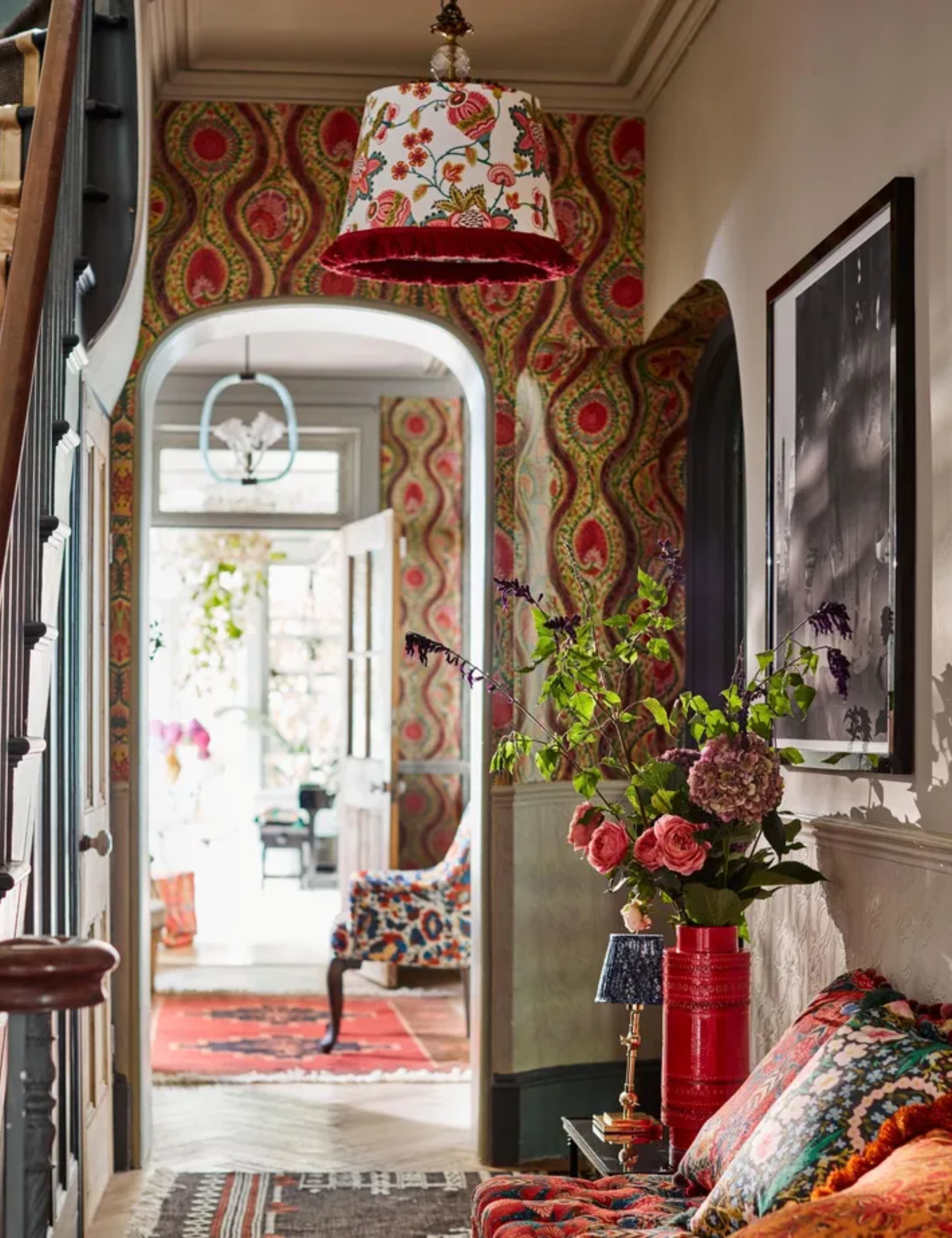 maximalist entryway with floral wallpaper, floral ceiling light, colorful rugs and colorful staircase with a patterned bench seat and patterned pillows