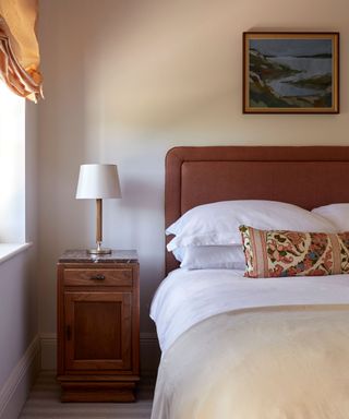 Neutral bedroom with a terracotta headboard, neutral bedding and a vintage bolster cushion