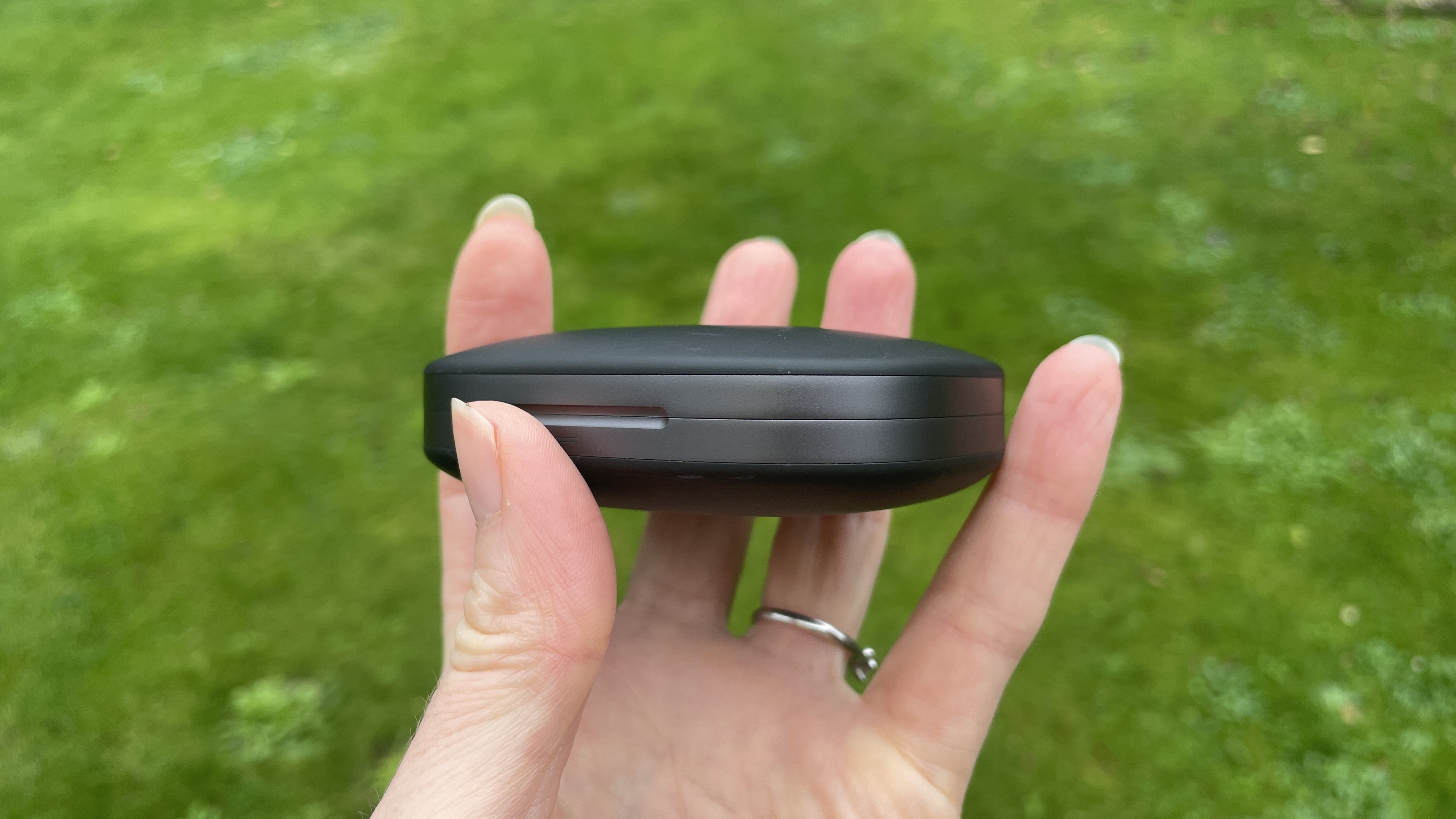 Shokz Openfit Pro outside, outside held in a woman's hand, with green grass in the background
